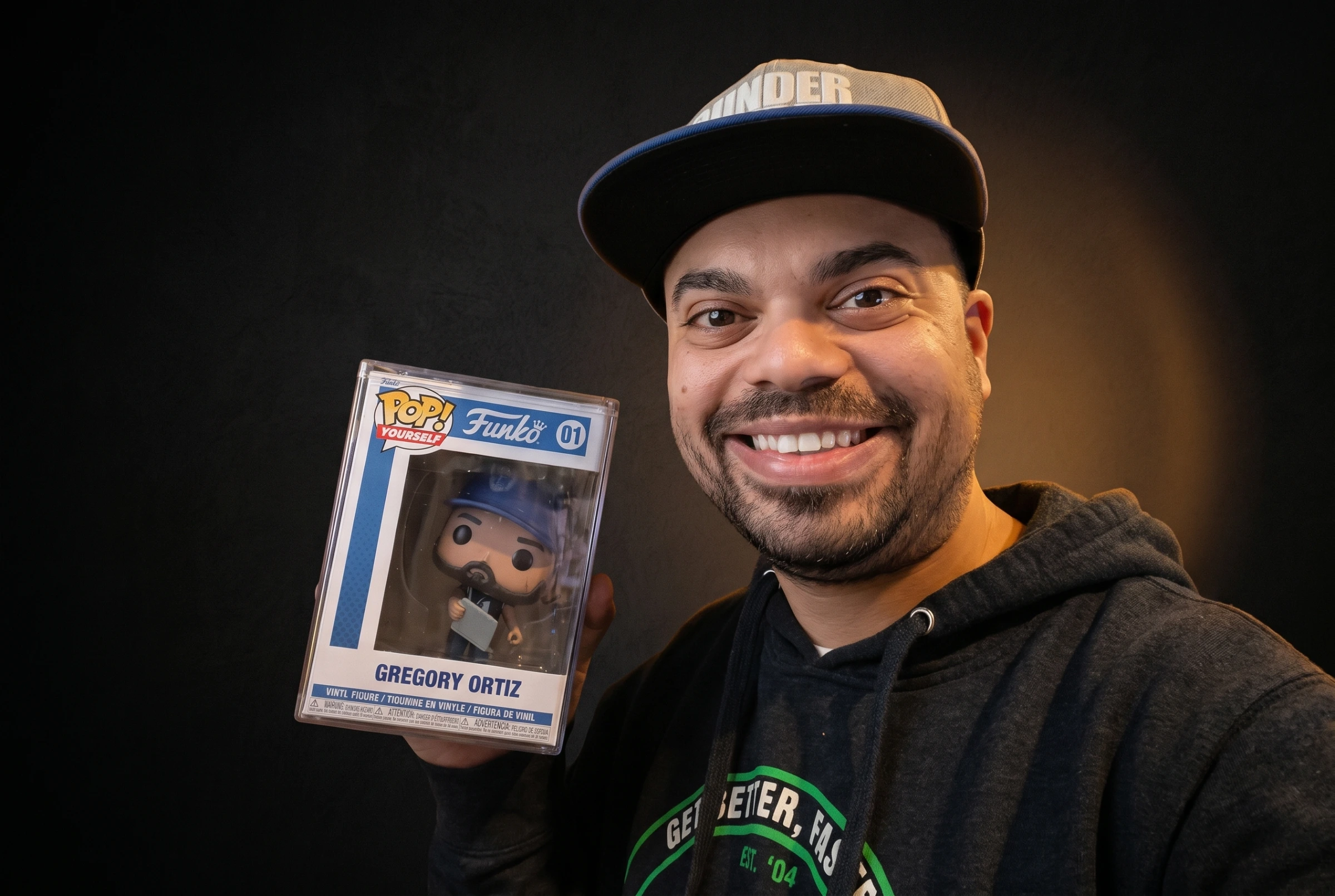 Gregory Ortiz smiling in his cap and holding his Funko collectible.